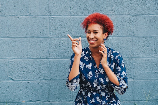 Image of a woman with red hair pointing at a blue wall and smiling